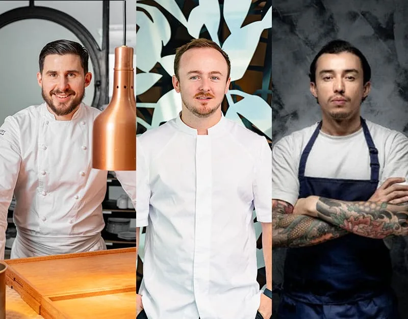 Three male chefs in white uniforms; the first is smiling by a counter, the second stands in front of a patterned background, and the third, with tattoos and a dark apron, stands with crossed arms before a textured wall.